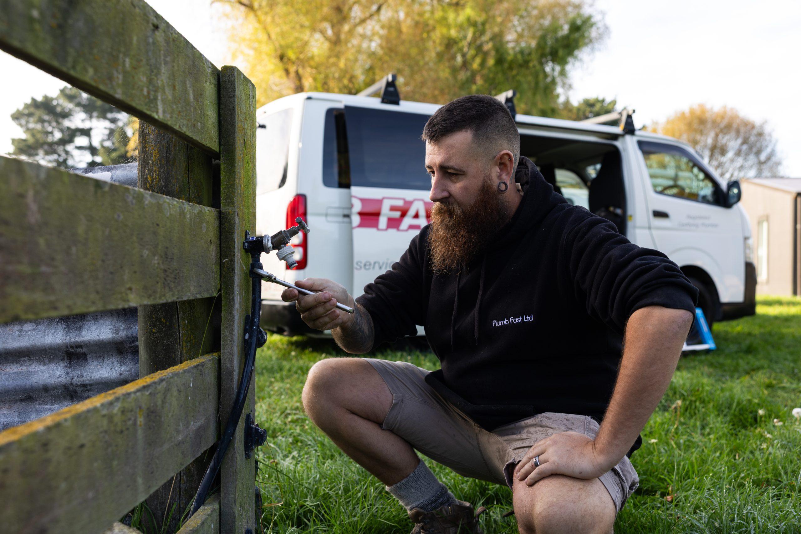Plumbfast plumber repairing an outdoor tap fitting with a service van behind