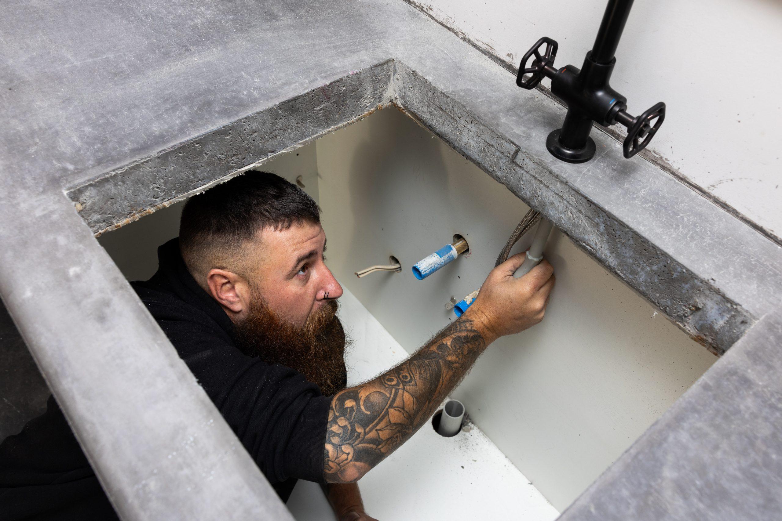 Plumbfast plumber working on pipework inside a concrete floor inspection pit